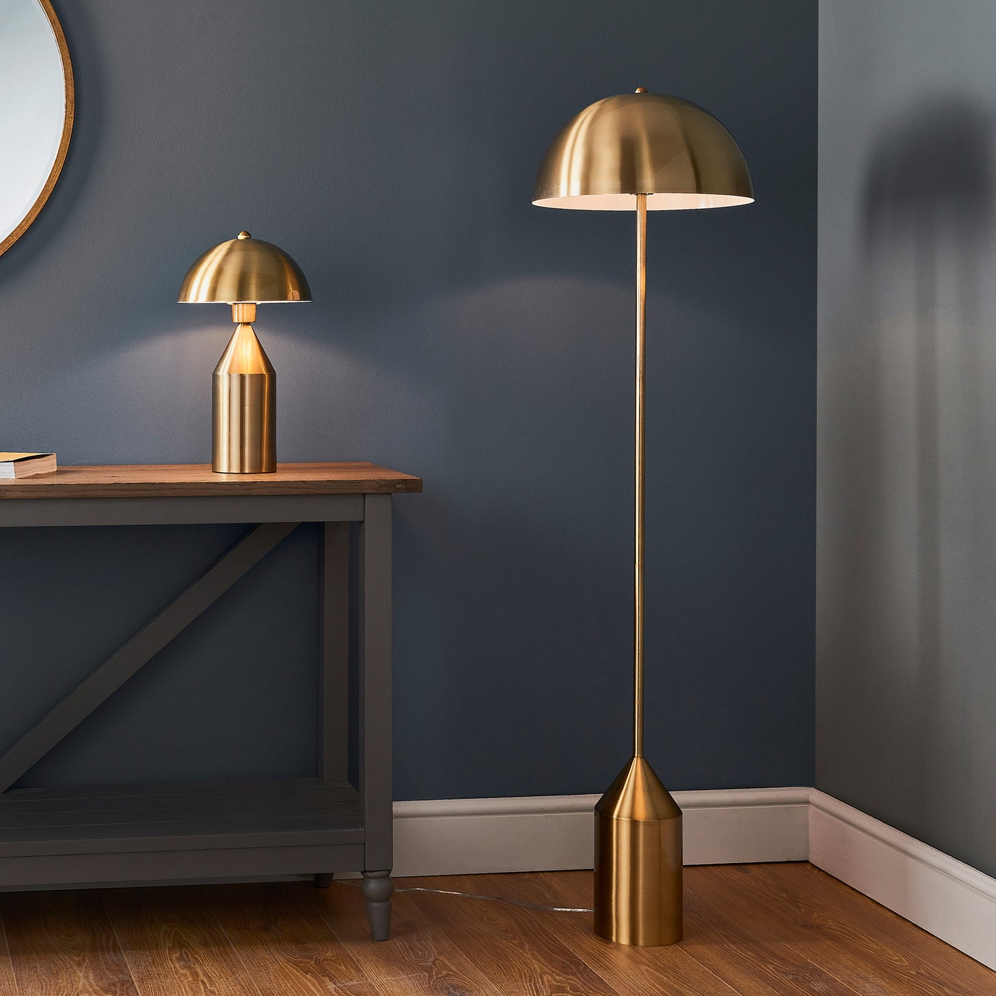 A Nova 1 Floor Light Antique Brass floor lamp next to a mirror, enhancing the interior decor of your home from Kikiathome.co.uk.