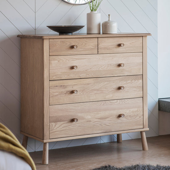 A Tigley 5 Drawer Chest in a bedroom, serving as home furniture and enhancing interior decor.
