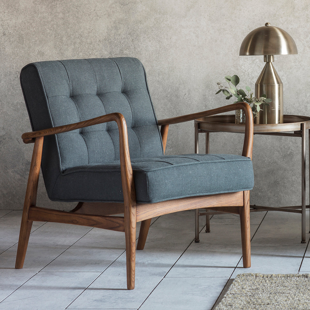 A Dark Grey Linen Camber Armchair with wooden legs and a lamp on a table, perfect for interior decor.