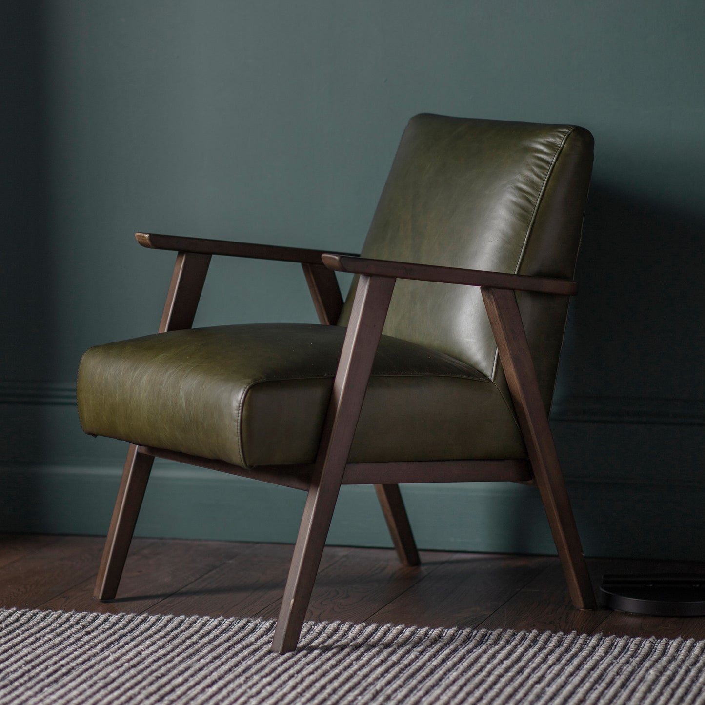 A Neyland Armchair in front of a green wall, perfect for interior decor.