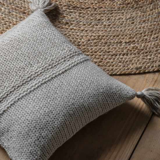 A Kikiathome.co.uk 2 Tone Knitted Cushion Oatmeal Cream 450x450mm with tassels, perfectly blending in as interior decor on a wooden table.