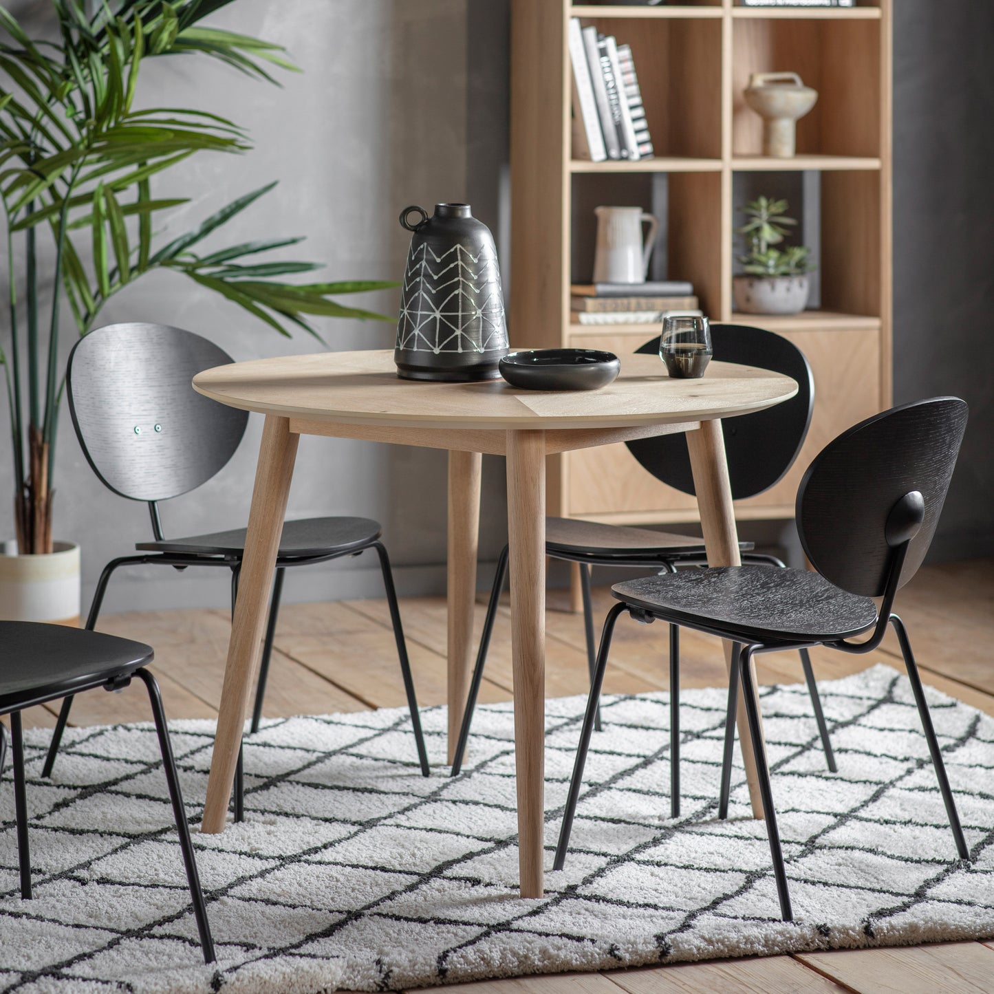 A Tristford Round Dining Table 1000x1000x700mm and chairs in a room with a plant, showcasing stylish home furniture and interior decor from Kikiathome.co.uk.