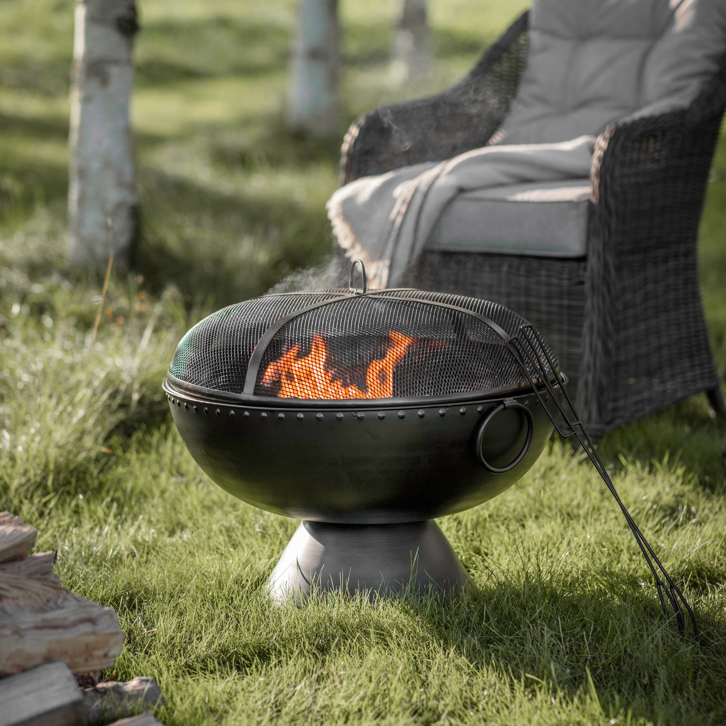 A Diptford Firepit from Kikiathome.co.uk, a home furniture and interior decor retailer, placed in the grass beside a chair.