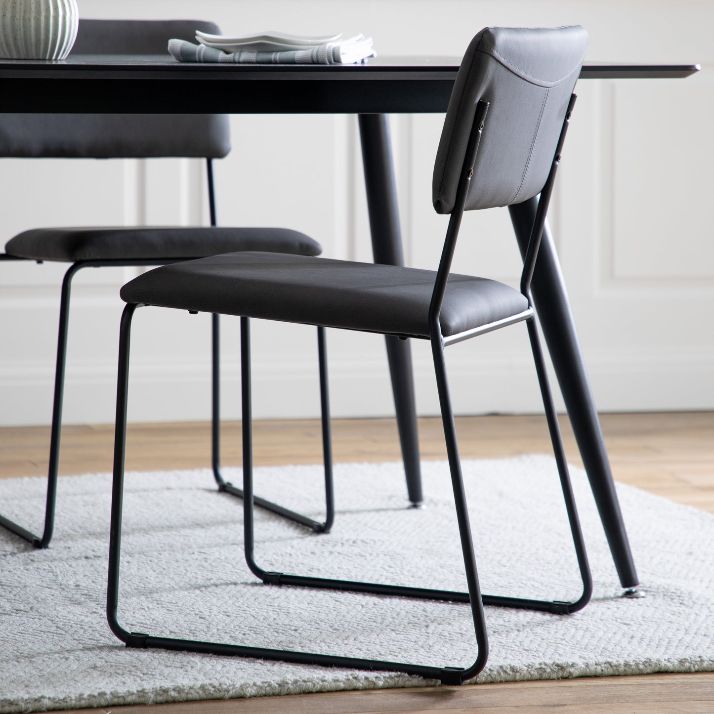 A Chivelstone Dining Chair Slate Grey (2pk) with two chairs and a black table for interior decor from Kikiathome.co.uk.