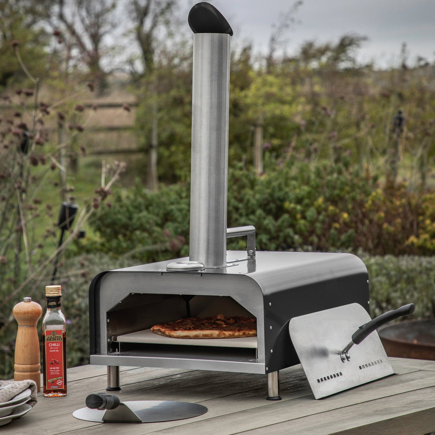 A Black Brixham Pellet Pizza Oven from Kikiathome.co.uk on an outdoor table for home decor.