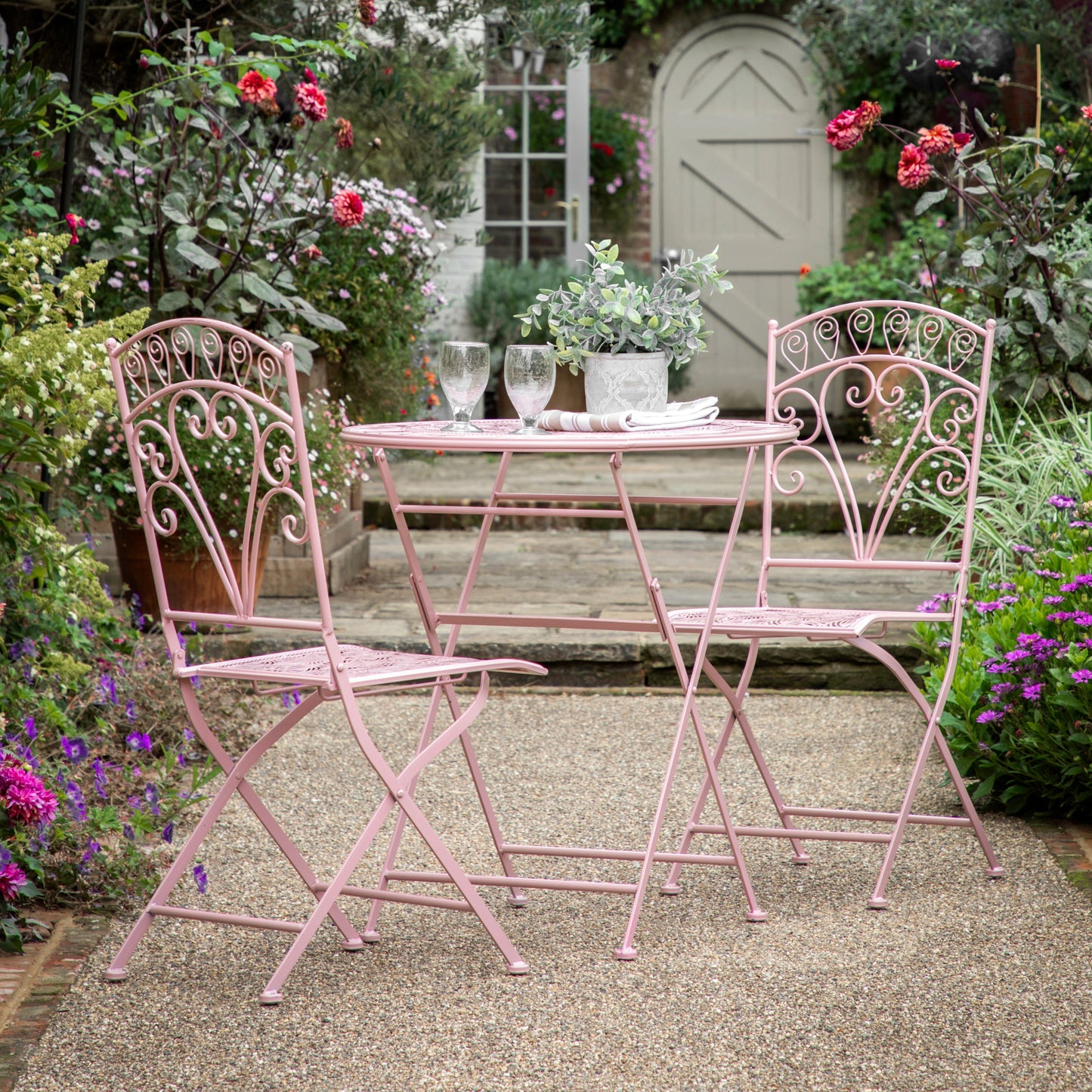 A Roborough 2 Seater Bistro Set Coral by Kikiathome.co.uk, perfect for interior decor or home furniture, displayed in a garden.