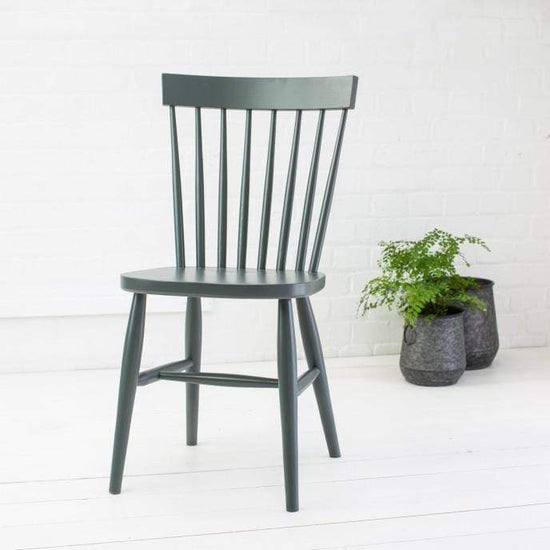 A pair of Kiki Painted Spindle Back Dining Chairs enhancing a white brick wall in home decor.