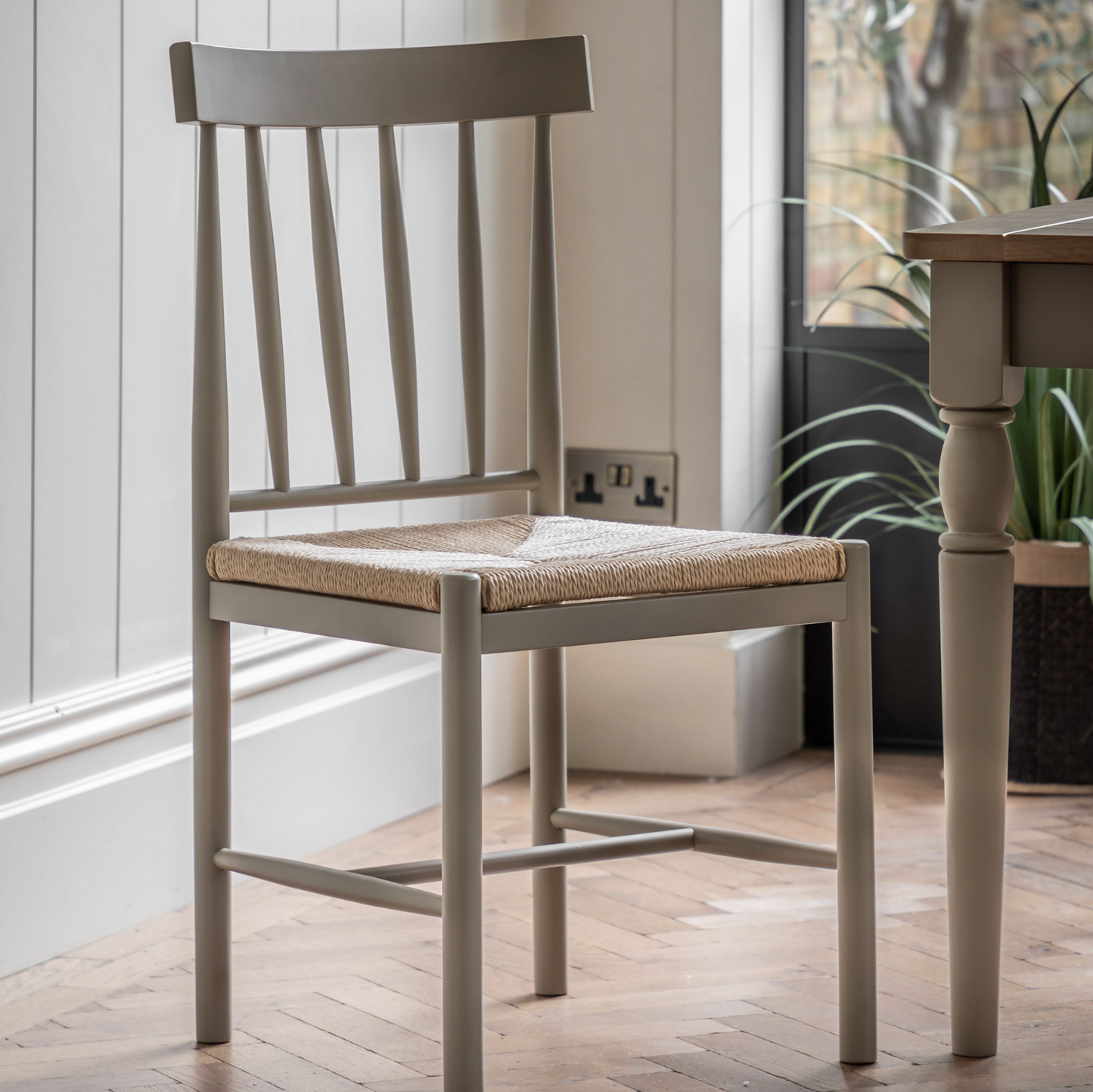 A Buckland Dining Chair 2pk in Prairie from Kikiathome.co.uk next to a wooden table, perfect for interior decor.