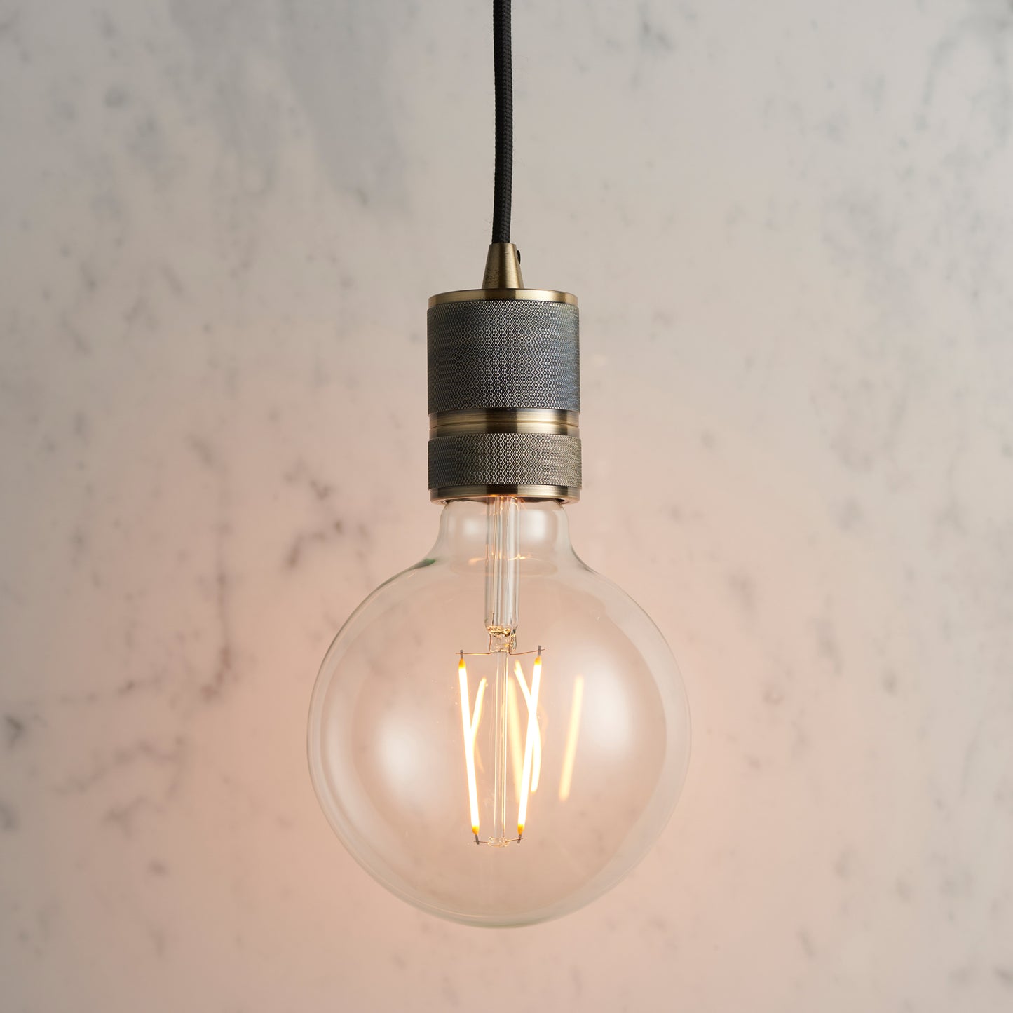 An Urban Pendant Light with an Antique Brass finish, hanging on a marble counter, perfect for interior decor.