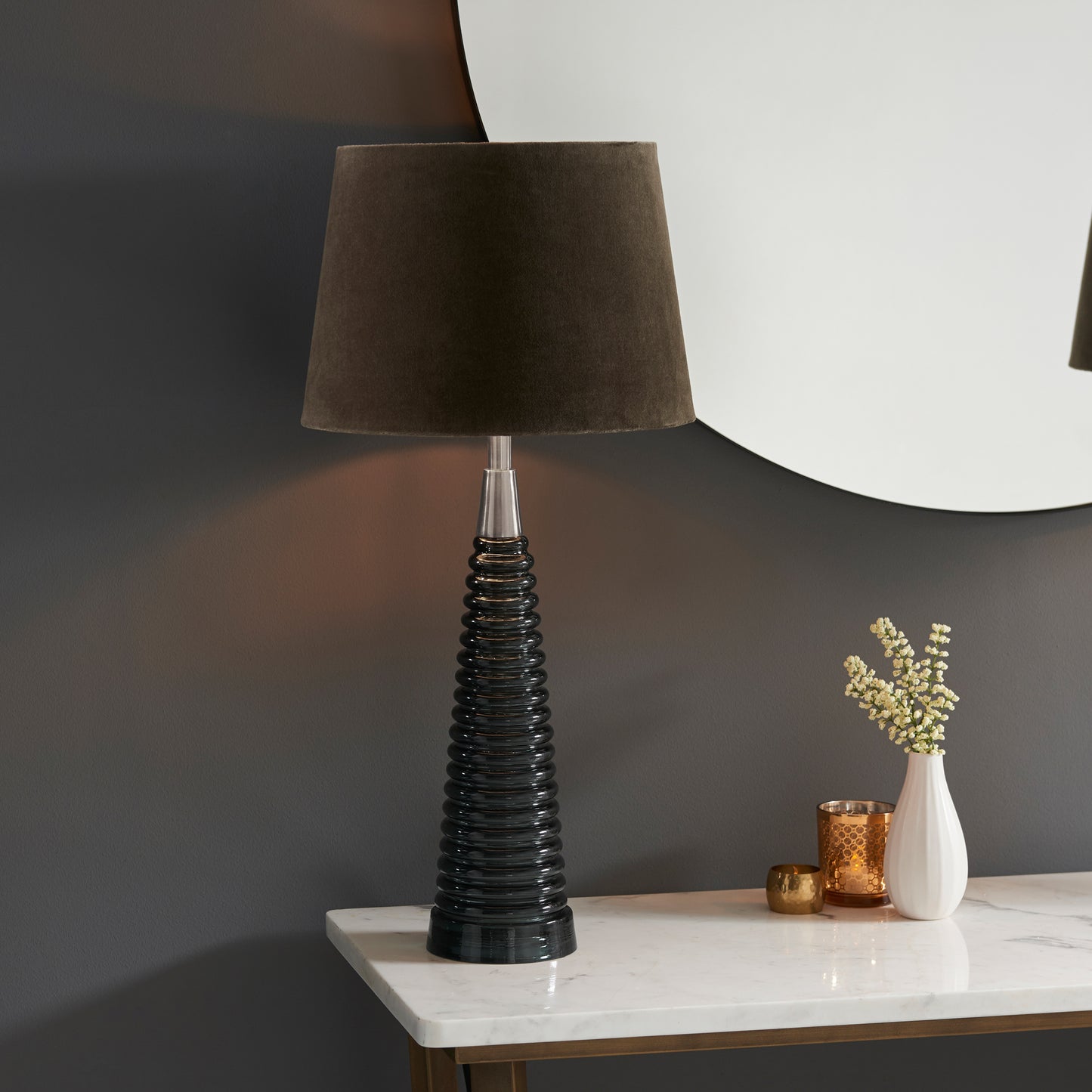 Load image into Gallery viewer, A sleek Naia 1 table lamp in light grey glass and mocha, perfect for interior decor and home furniture, adorns a table next to a mirror from Kikiathome.co.uk.
