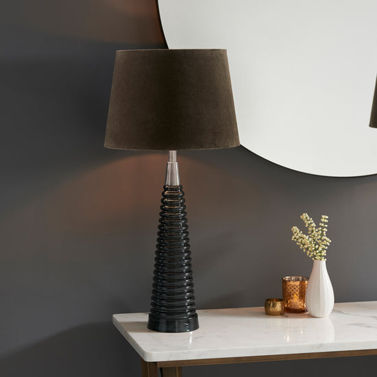 A sleek Naia 1 table lamp in light grey glass and mocha, perfect for interior decor and home furniture, adorns a table next to a mirror from Kikiathome.co.uk.