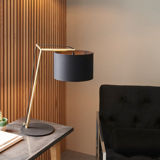 A Buckland Table Lamp in Antique Brass and a black shade perfectly complements a black chair, creating an elegant interior decor for your home furniture.