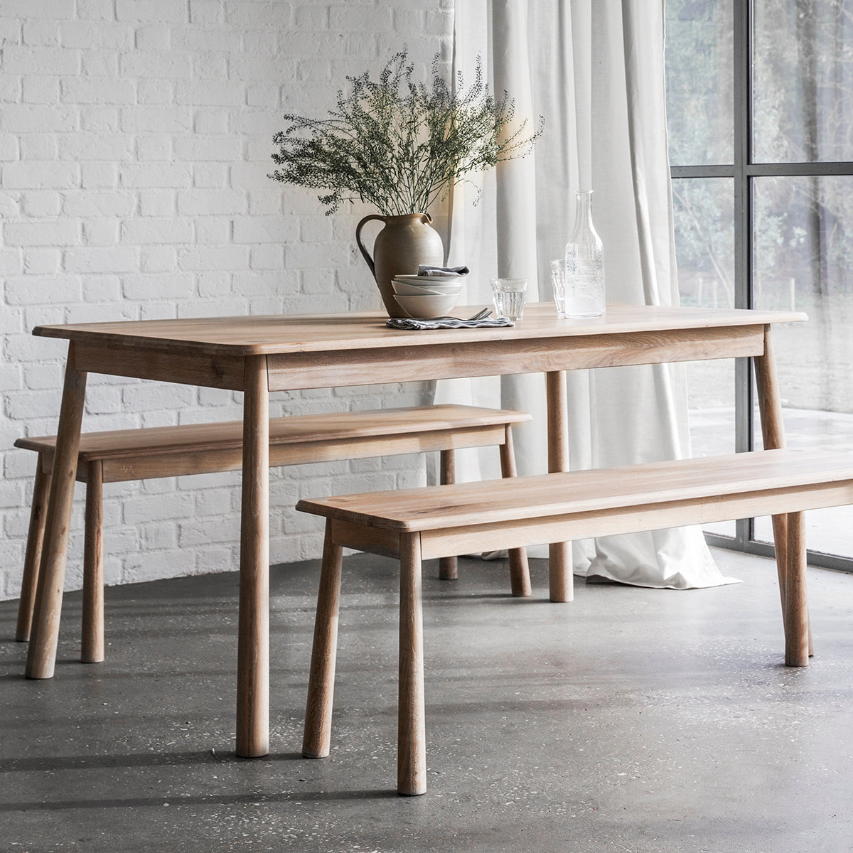 A Tigley Dining Table and bench from Kikiathome.co.uk enhances the interior decor of a room with a window.