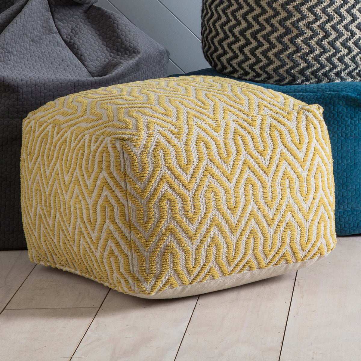 A Stromstad Pouffe Ochre sitting on a wooden floor, adding elegance to the interior decor of your home.