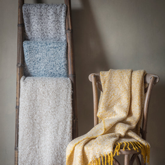 A ladder with a Herringbone Faux Mohair Throw Grey 1300x1800mm, perfect for interior decor.