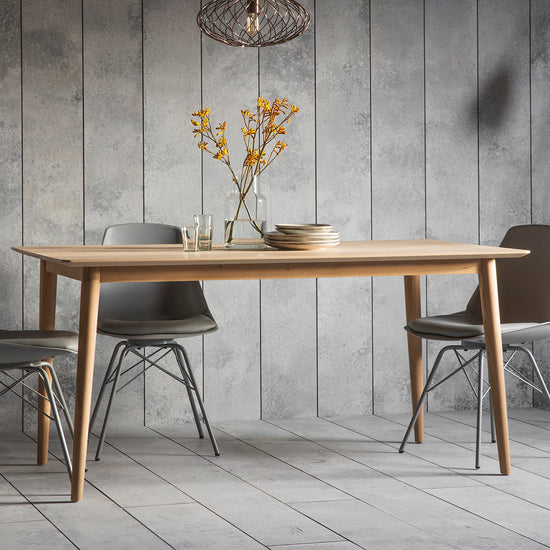 A Tristford Dining Table 1600x900x760mm and chairs in a room with grey walls, showcasing exquisite home furniture and interior decor from Kikiathome.co.uk.