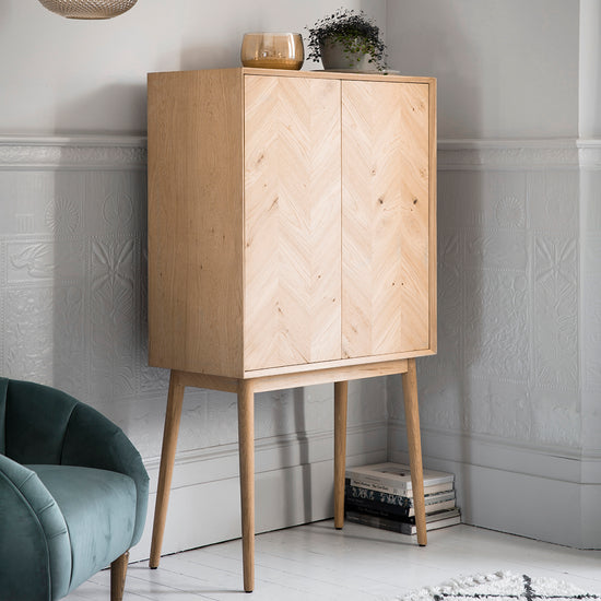 A Tristford 2 Door Cocktail Cabinet, a stylish addition to your interior decor, positioned next to a chair in a room, available at Kikiathome.co.uk.
