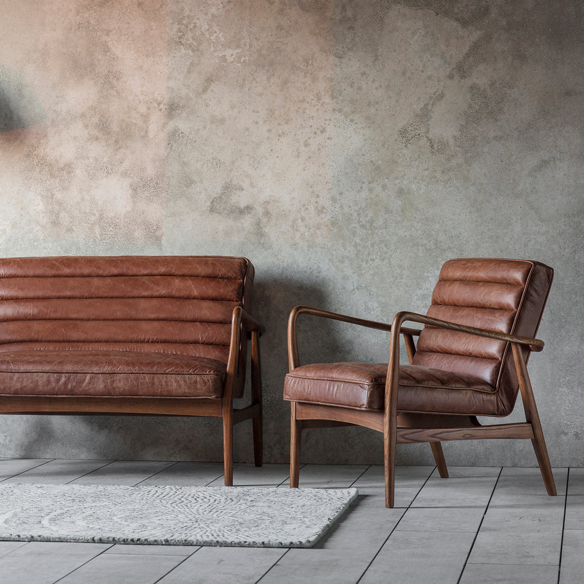 A pair of vintage brown leather armchairs from Kikiathome.co.uk in front of a concrete wall, perfect for interior decor.