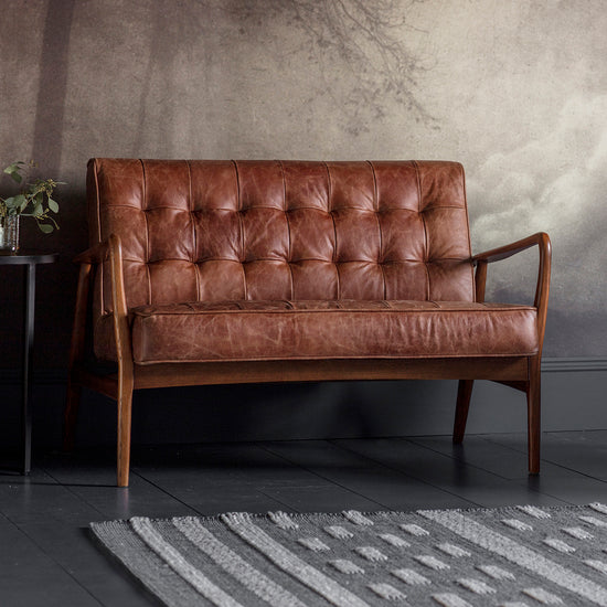 A vintage brown leather 2 seater sofa from Kikiathome.co.uk in front of a wall, adding elegance to interior decor.