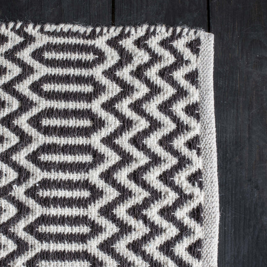 Load image into Gallery viewer, Home furniture - A Charleton Rug Black &amp;amp; Cream 1600x2300mm from Kikiathome.co.uk beautifully enhances interior decor on a wooden floor.
