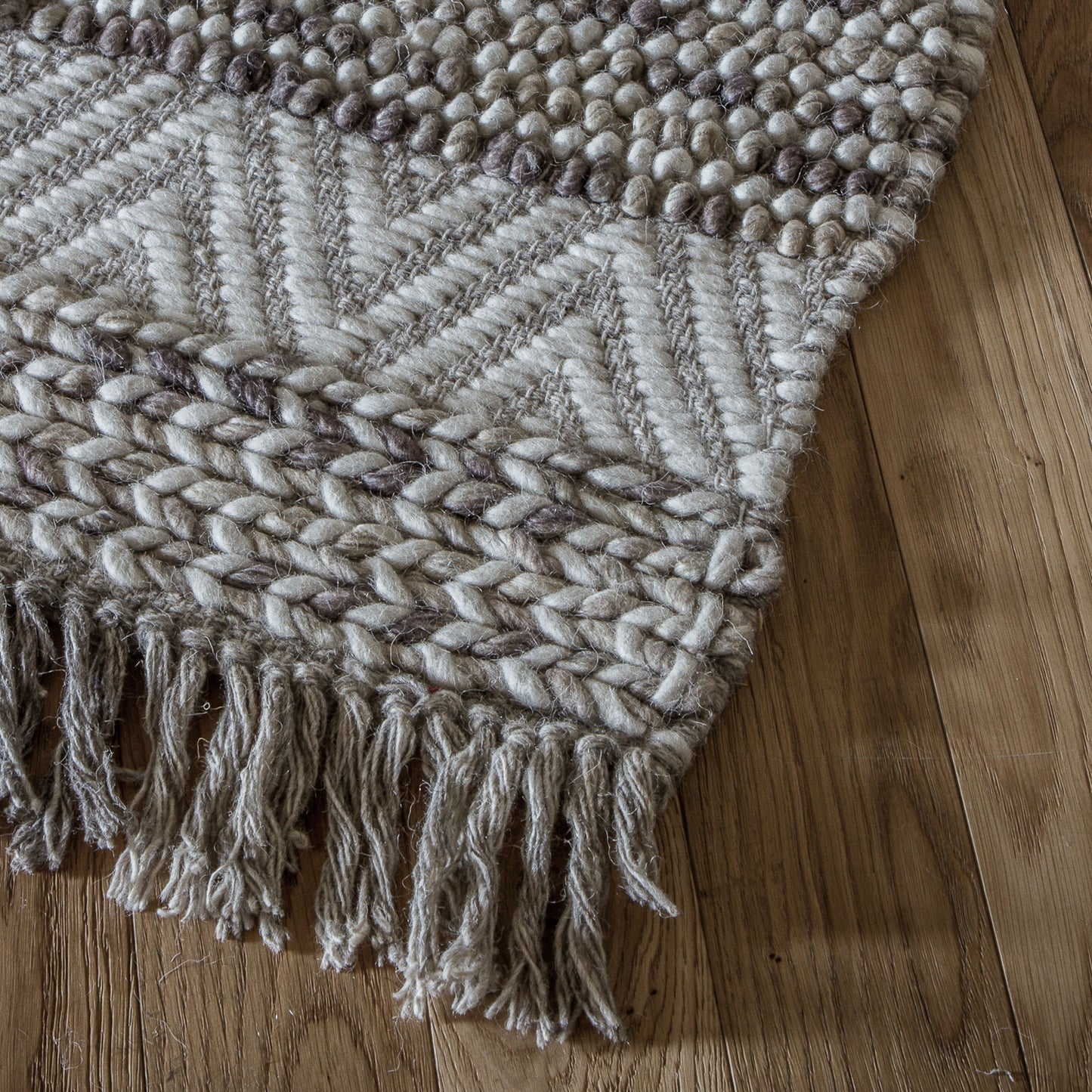 A Ludiene Rug Ivory 1600x2300mm with fringes on a wooden floor for home interior decor.