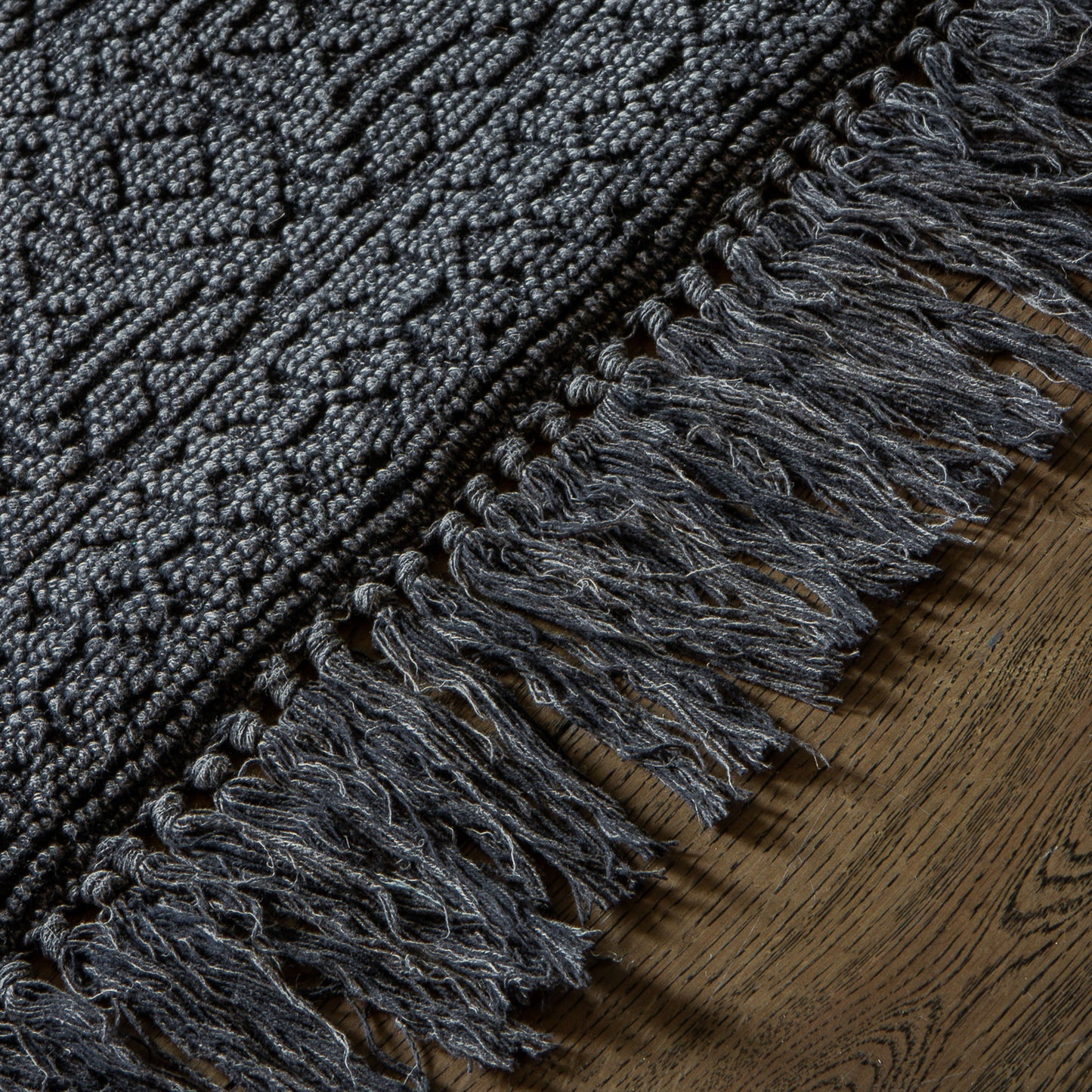 A charcoal rug with fringes on a wooden floor from Kikiathome.co.uk, adding warmth and style to your interior decor.