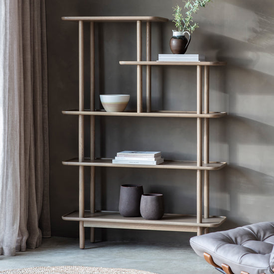 An Interior decor shelf, the Wembury Open Display Grey 1100x380x1600mm shelf from Kikiathome.co.uk, is showcased in a room with a chair and a