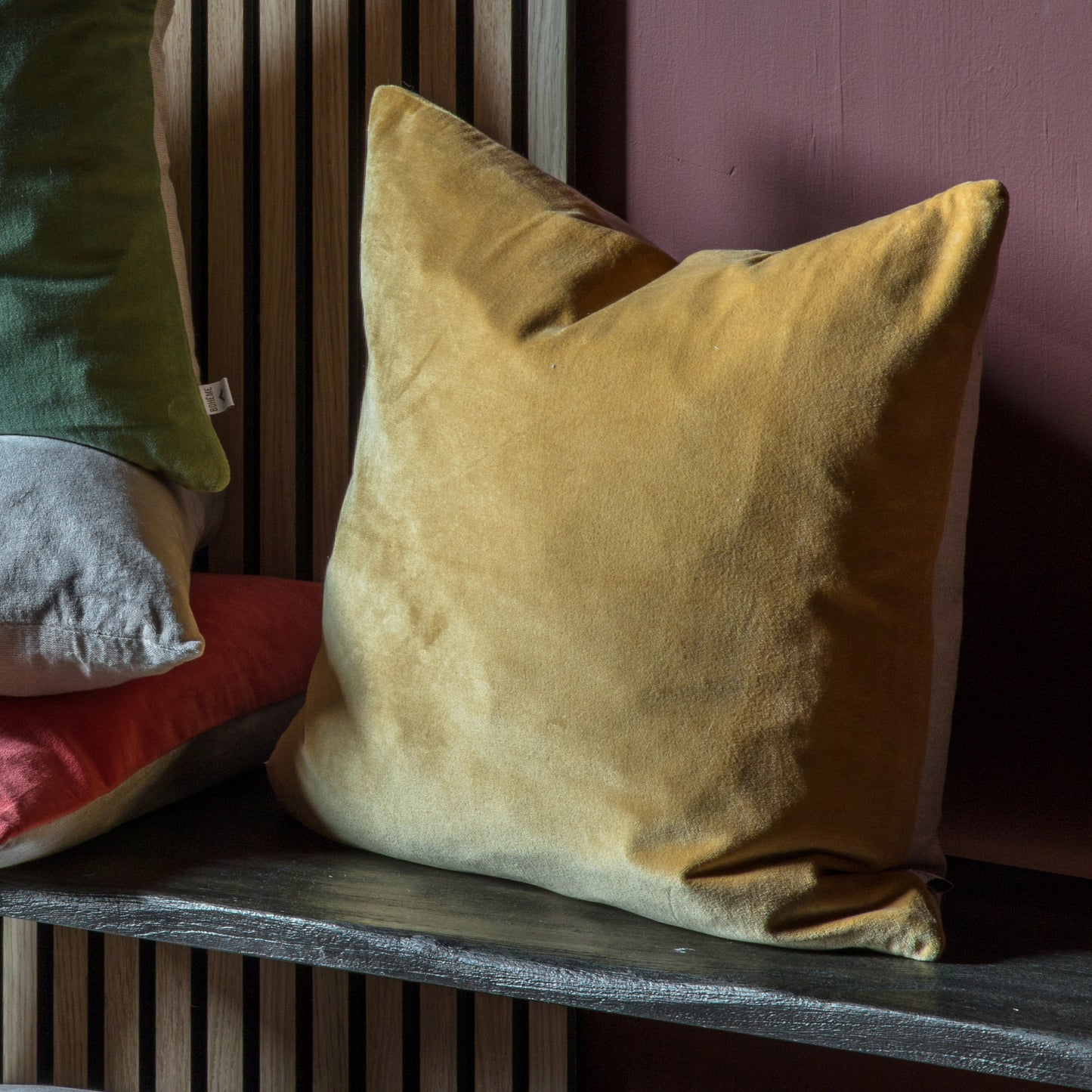 A group of Cotton Velvet Cushion Mustard 500x500mm pillows, part of the home furniture collection, sitting on a shelf next to a wall by Kikiathome.co.uk.