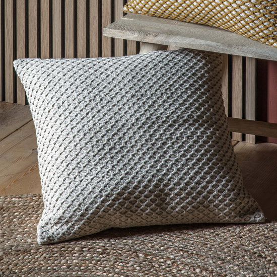 A Bittaford Cushion Natural 550x550mm for interior decor from Kikiathome.co.uk on a wooden floor.