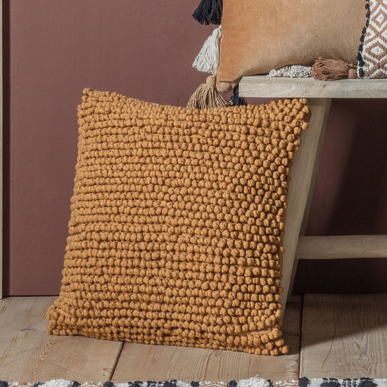 A Pino Cushion Tan 450x450mm with a pom pom on it for interior decor.