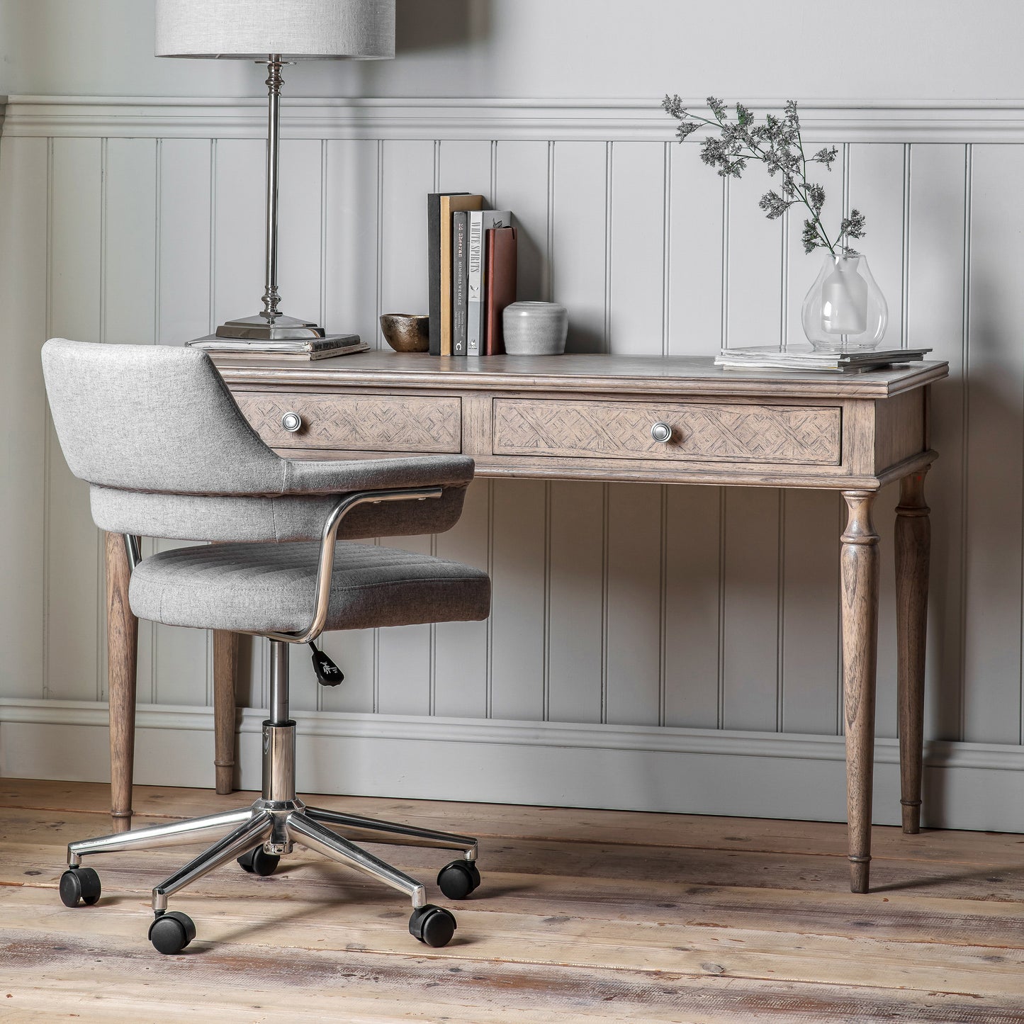 A Belsford 2 Drawer Desk 1300x600x780mm in an interior decor setting with a lamp and a chair.