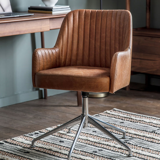 A vintage brown leather Curie Swivel Chair complements the interior decor of a home, placed on a rug in front of a desk from Kikiathome.co.uk.