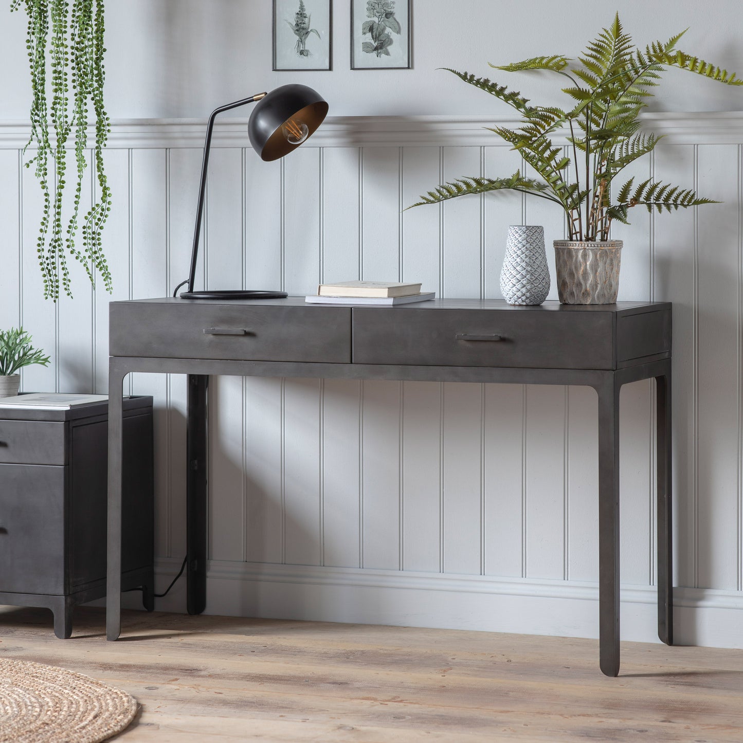 A grey Ottinge 2 Drawer Desk 1200x450x790mm with two drawers and a plant for interior decor.