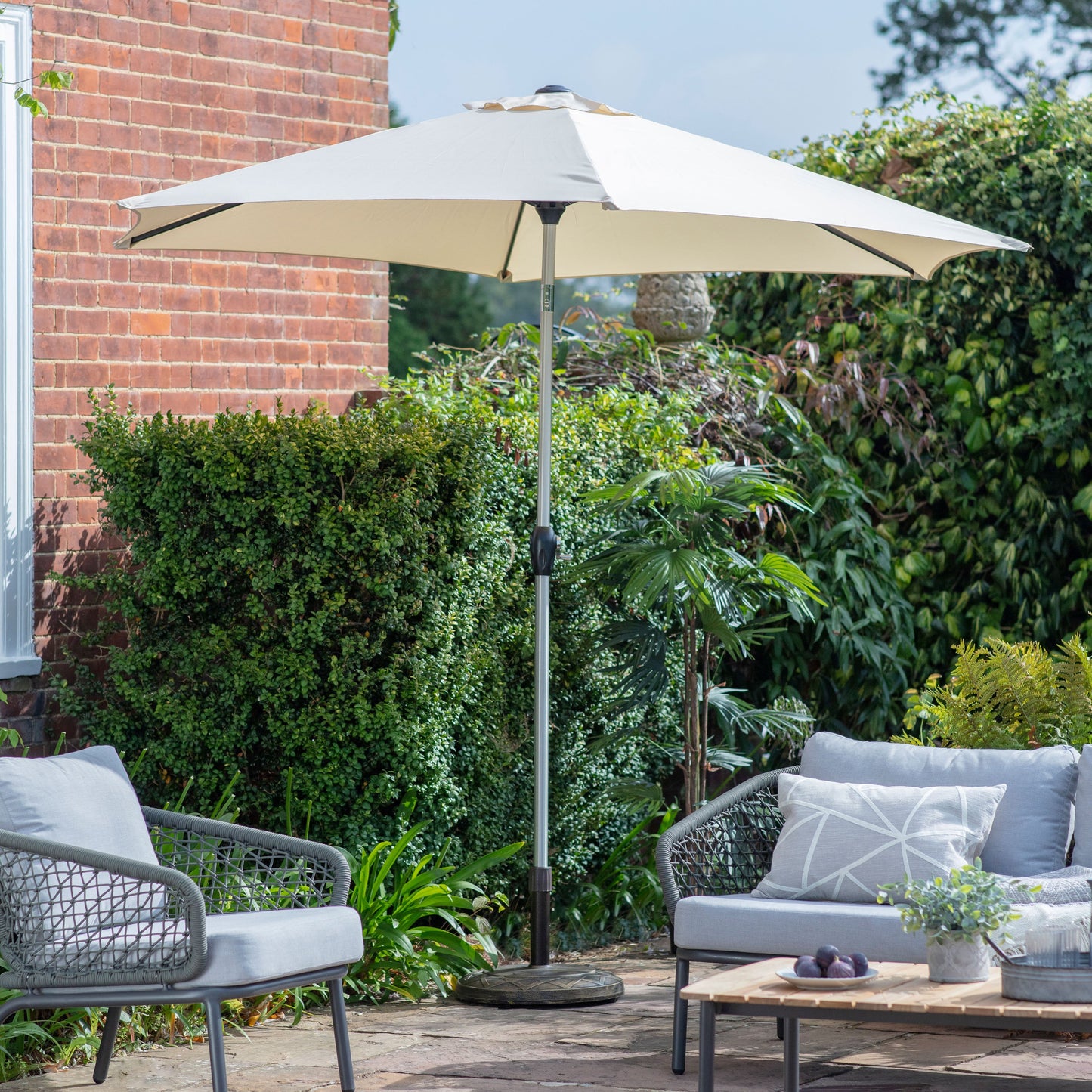 A patio featuring a Kikiathome.co.uk Alwington 2.7m Parasol Cream umbrella and stylish grey furniture from home furniture.
