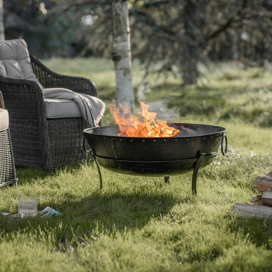 A Thurlstone Firepit surrounded by wicker furniture in a grassy area, perfect for interior decor.