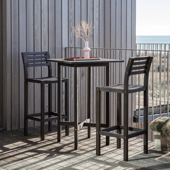 Two Alfrington 2 Seaters High Bar Set Black by Kikiathome.co.uk and a table on a balcony overlooking the ocean, perfect for home furniture and interior decor.