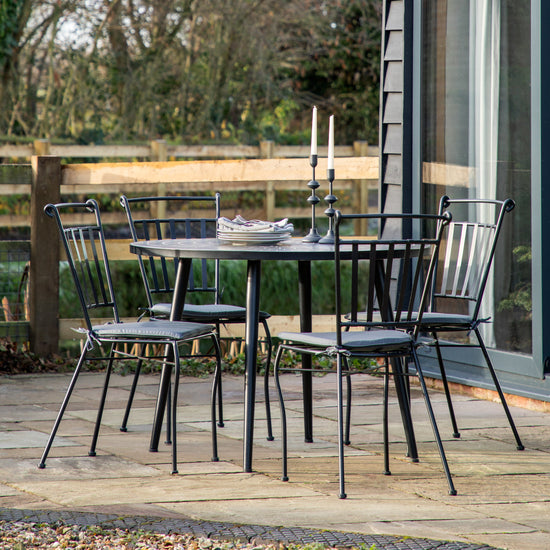 A black Haytor Mosaic Round Dining Table and chairs on a patio for interior decor.