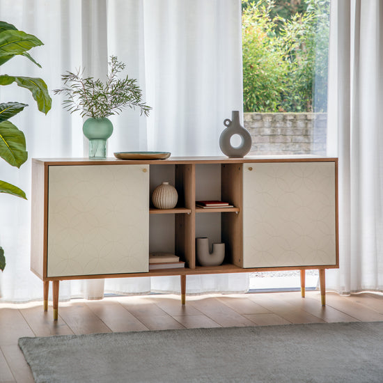 A Newbury Sideboard Oak White adds charm to the interior decor of a living room with a plant on it.
