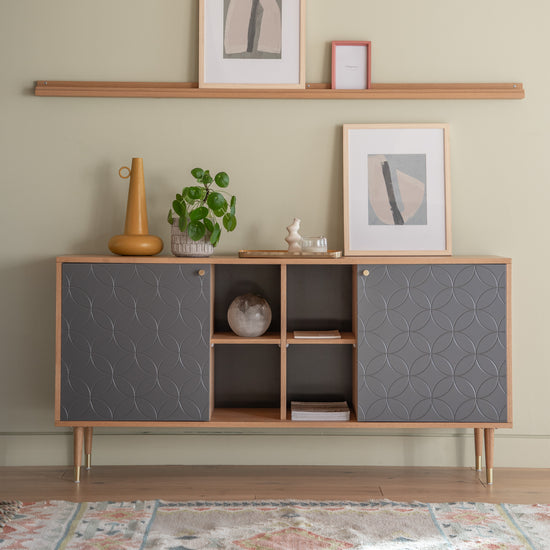 A grey Newbury Sideboard Oak Grey 1600x400x790mm with shelves and a plant on top for interior decor.