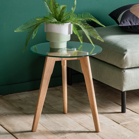 A home furniture, Kikiathome.co.uk Ashprington Round Side Table Oak 450x450x500mm with a plant on it next to a green wall for interior decor.