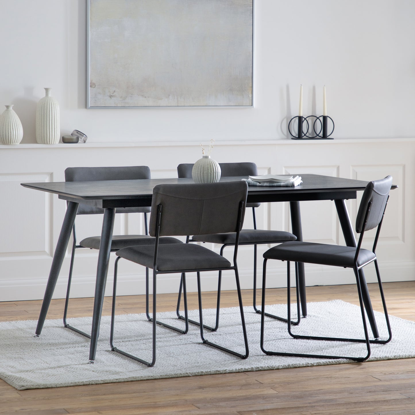 An Ashford Dining Table Black 1600x900x750mm with four chairs and a rug for interior decor.