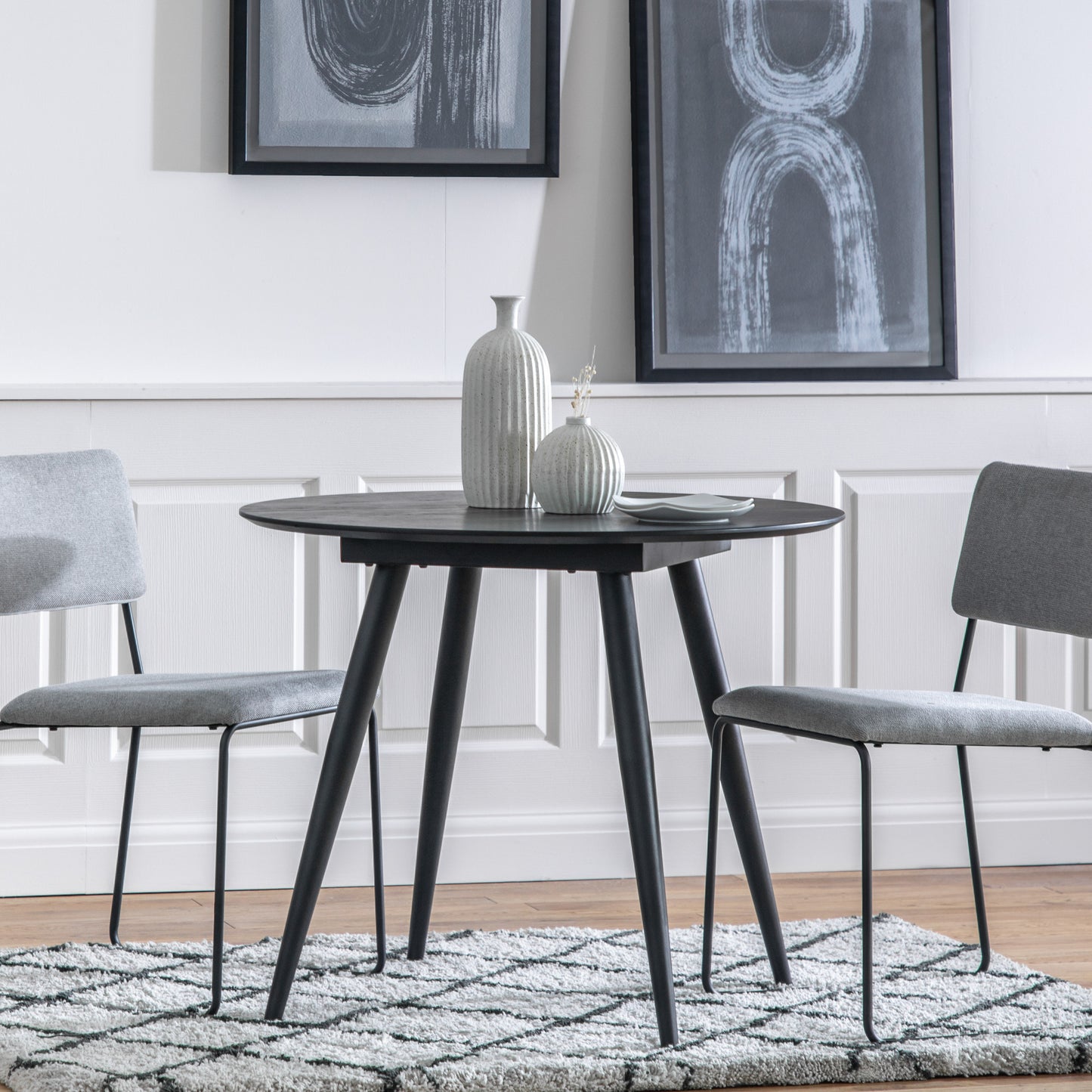 An Ashford Round Dining Table Black with two grey chairs for interior decor from Kikiathome.co.uk.