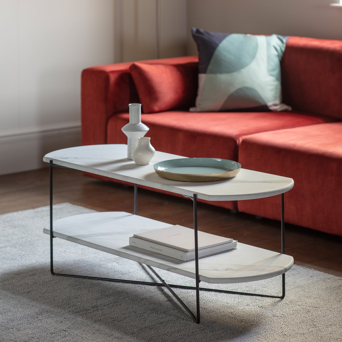 A Linford Display Coffee Table Wht Marble 1100x420x450 with a faux white marble top in a living room with a red couch, available at Kikiathome.co.uk.