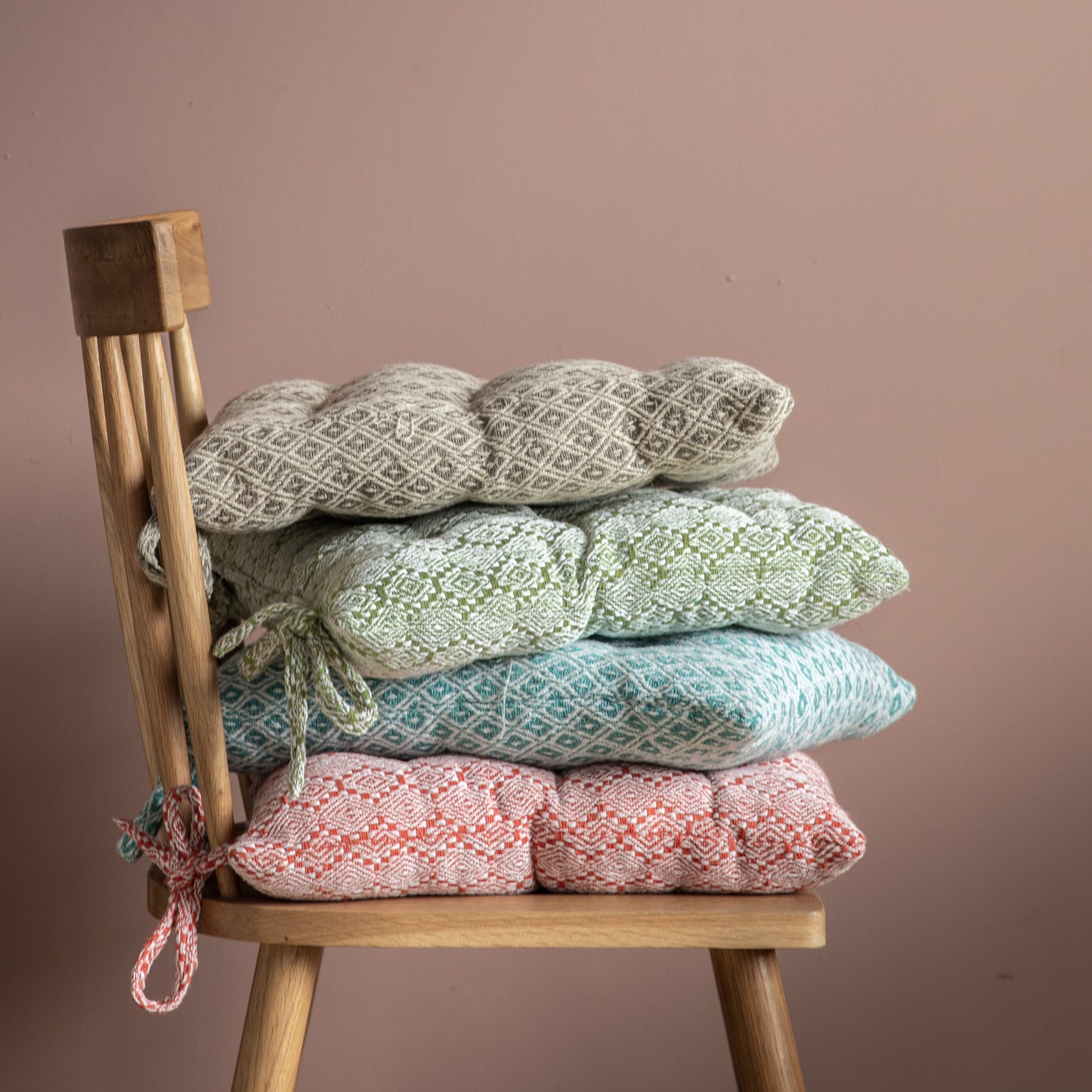 A stack of taupe seatpad pillows on a wooden chair from Kikiathome.co.uk, adding style to your home furniture.