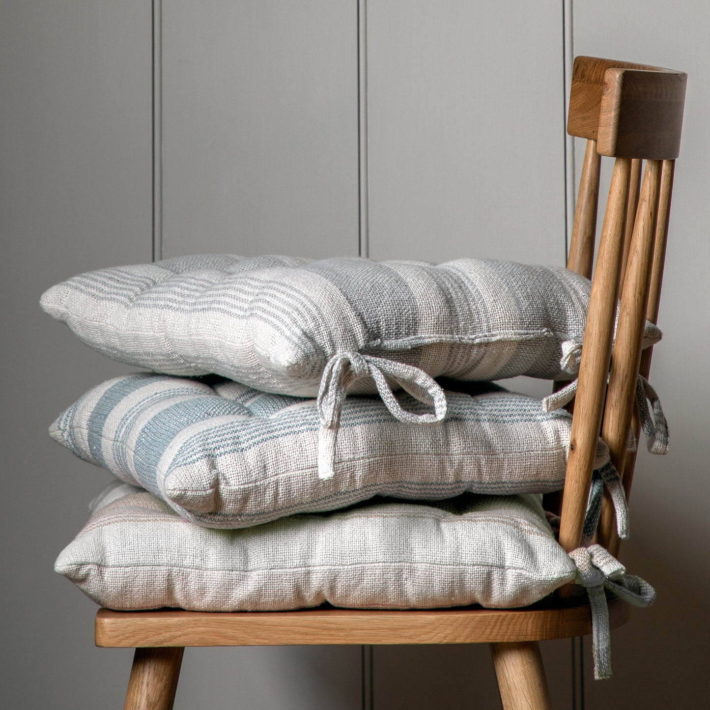 Four Simply Organic Str Seatpad Taupe 430x430mm (2pk) stacked on a wooden chair for interior decor.