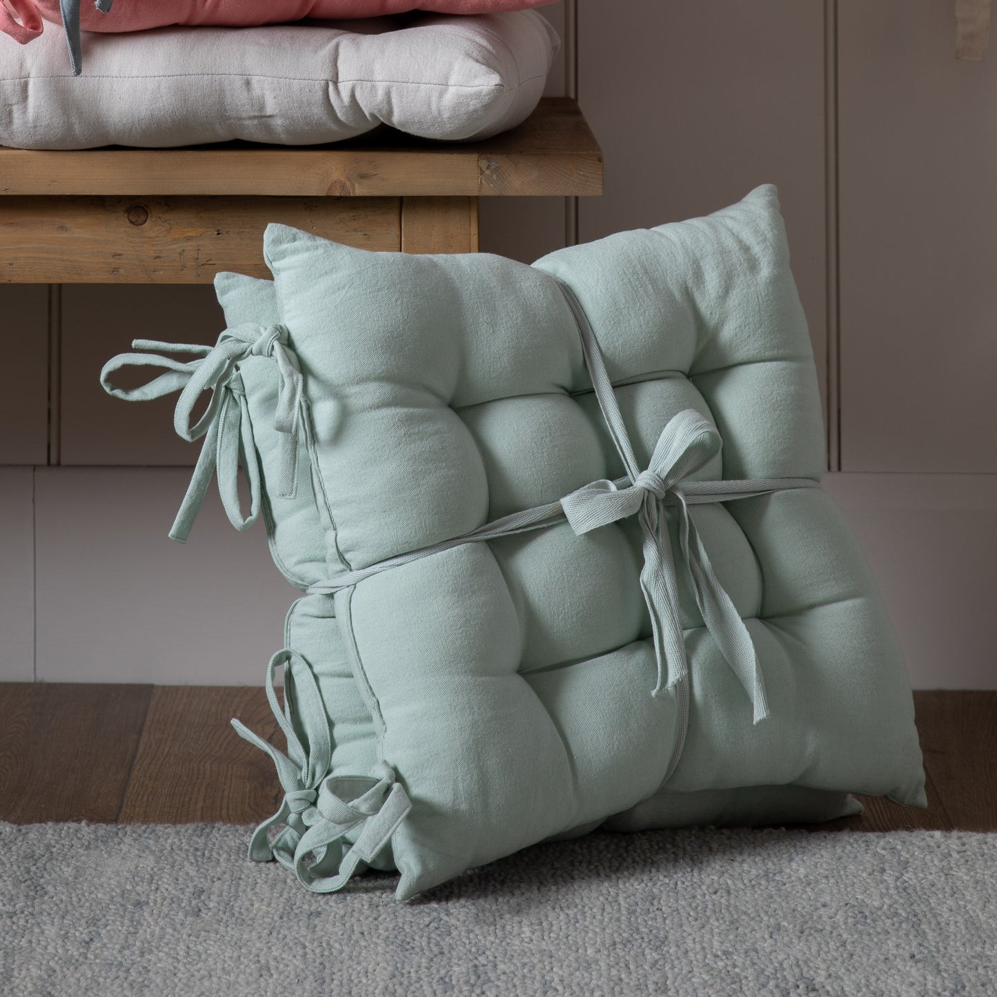 A set of SC Plain Cotton Seatpad Aqua 430x430mm (2pk) pillows on a wooden floor adding to the interior decor of the home.