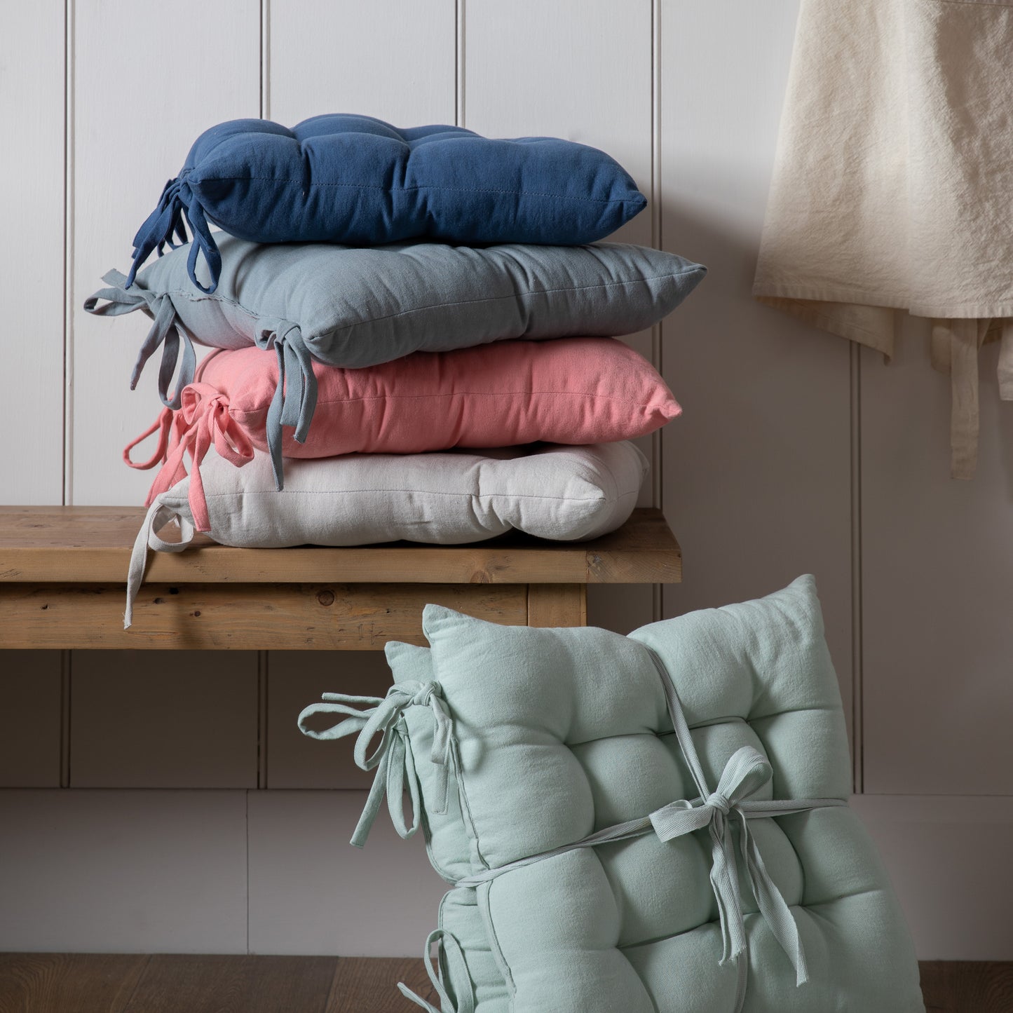 A stack of SC Plain Cotton Seatpad pillows on top of a wooden bench from Kikiathome.co.uk, adding a touch of interior decor to the home furniture.