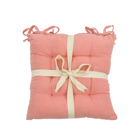A stylish SC Plain Cotton Seatpad Coral 430x430mm (2pk) adorned with a decorative ribbon, perfect for interior decor.