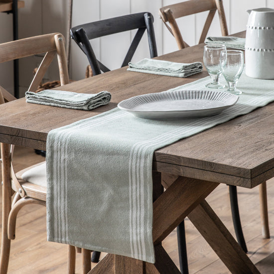 A dining room table adorned with a Stripe Reversible Table Runner Sage 360x1800mm, enhancing the interior decor of the home.