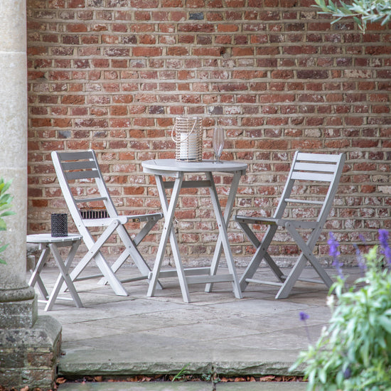 A Chillington Folding Chair Whitewash (2pk) and table, perfect for interior decor and home furniture, placed on a brick patio.